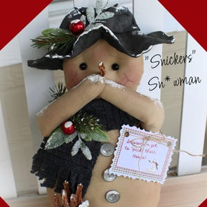 May include: A handmade snowman doll with a black hat, scarf, and mittens. The snowman has a carrot nose, button eyes, and a tag that says "Snowmen get to 'pick' their noses!" The doll is decorated with faux greenery and berries.