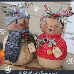 May include: Two handmade Christmas ornaments, a snowman and a girl, both wearing winter clothing. The snowman is wearing a gray scarf and hat, and the girl is wearing a red sweater and a plaid headband. Both ornaments have a rustic, vintage look and are decorated with holly and pine cones. The ornaments are labeled "Snowman Pep" and "Magic Elf".