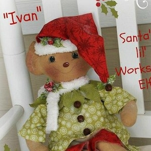 May include: A handmade elf doll named "Ivan" wearing a red hat, green and white patterned dress, and green shoes. The doll is sitting on a white chair with a sign that reads "Santa's lil Workshop Elf".