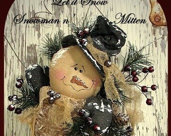 May include: A handmade snowman ornament with a red mitten, a brown burlap hat, and a brown burlap scarf. The ornament is decorated with berries and greenery. The text "Let it Snow Snowman n' Mitten Old Road Primitives 2009" is written on the background.