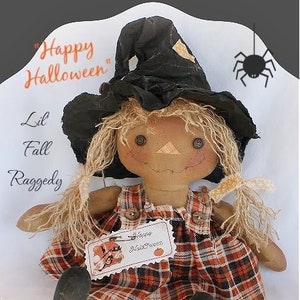 Puede incluir: Muñeca de trapo hecha a mano con sombrero de bruja negro y vestido a cuadros. La muñeca tiene ojos de botón, pelo de paja y una etiqueta que dice "Happy Halloween". Decoración temática de otoño.
