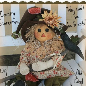 May include: A handmade country scarecrow doll with a brown hat, a crocheted lace collar, and a floral print dress. The doll is sitting on a white bench with a black bird perched on a stick. The text "Why can't we be friends?" is written on the bench. The text "Country Scarecrow" and "Old Road Primitives" is also visible in the image.