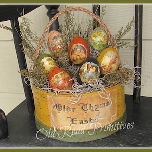 Peut inclure: Un récipient en métal peint en jaune et vert avec une poignée en corde rempli d'œufs de Pâques décoratifs. Le récipient porte une étiquette sur laquelle est inscrit "Olde Thyme Easter Old Road Primitives".