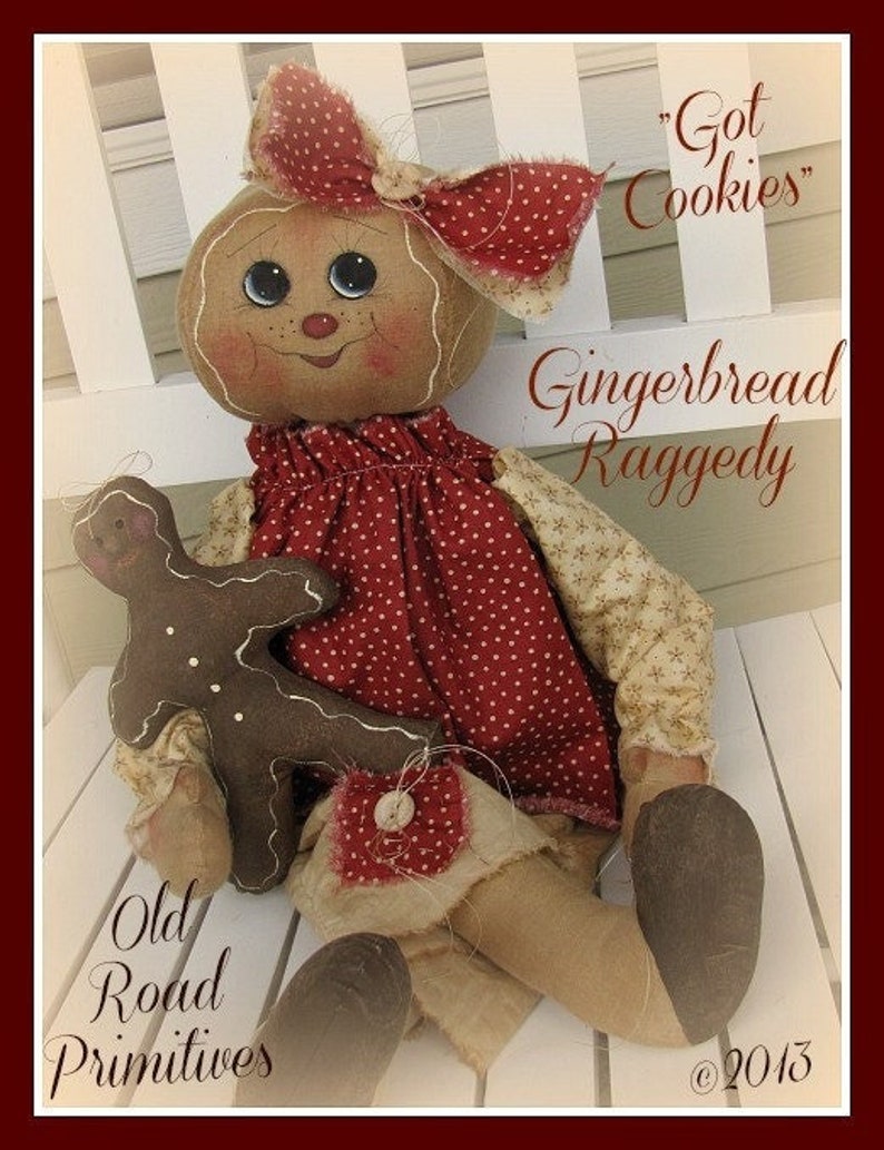 May include: A gingerbread rag doll with a red and white polka dot dress and a brown gingerbread cookie in her arms. The doll is sitting on a white bench and has a red bow in her hair. The text "Got Cookies" and "Gingerbread Raggedy" is written on the image. The text "Old Road Primitives" and "&copy;2013" is also written on the image.