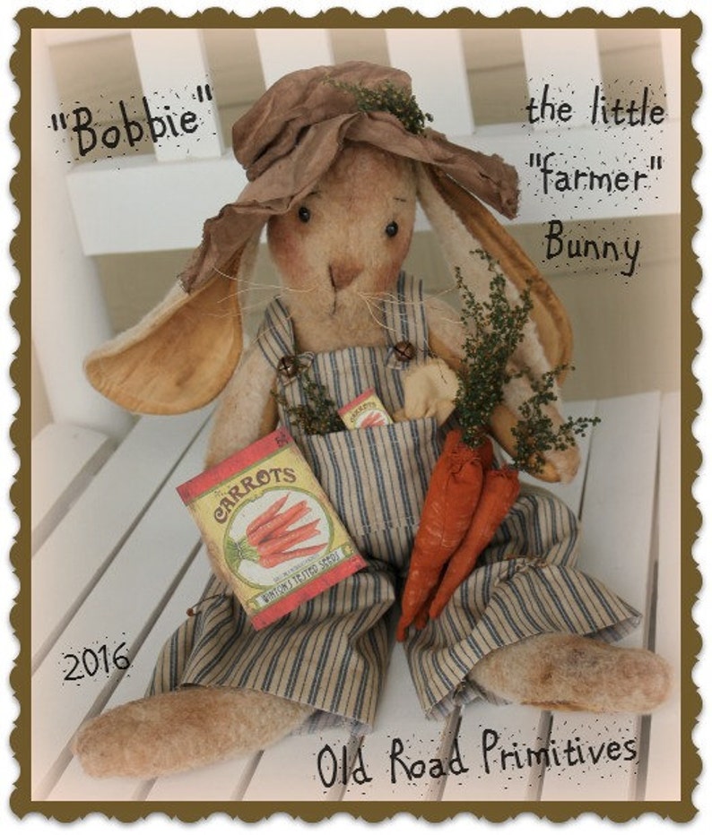 May include: A handmade plush bunny doll dressed as a farmer, wearing overalls, a straw hat, and holding a bag of carrot seeds and carrots. The doll is sitting on a white bench and has the text "Bobbie" and "the little "farmer" Bunny" written above it. The text "2016" and "Old Road Primitives" are written below the doll.