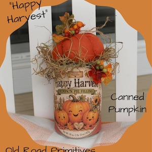 May include: A decorative tin can labeled Happy Harvest Pumpkin Pie Filling with a graphic of three smiling pumpkins. The top is adorned with a fabric pumpkin, dried straw, and artificial autumn leaves. The label includes the text Net Wt. 29 oz. (1 lb. 13 oz.) 822g.