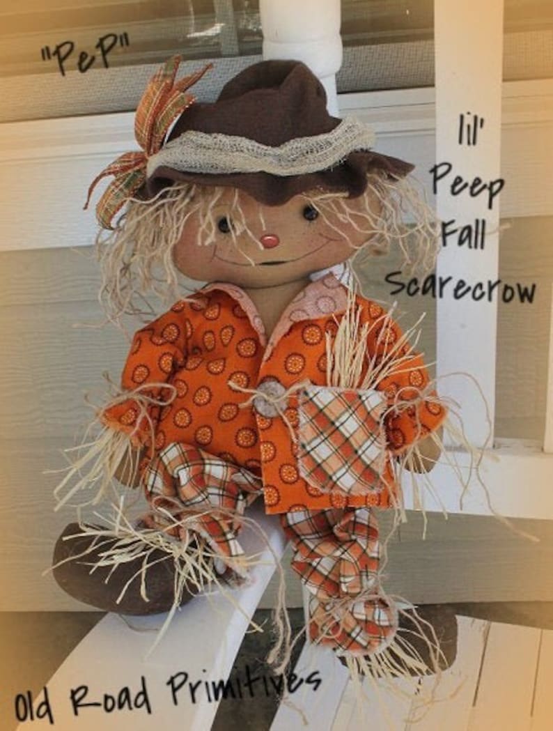 Puede incluir: Una mu&ntilde;eca de espantap&aacute;jaros de oto&ntilde;o hecha a mano con un sombrero de fieltro marr&oacute;n, pantalones de cuadros naranja y blanco y un bolsillo lleno de paja. La mu&ntilde;eca est&aacute; etiquetada como "Lil' Peep Fall Scarecrow" y "Old Road Primitives".