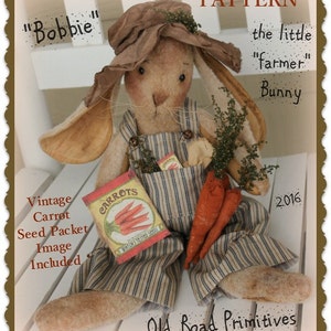 May include: A handmade bunny doll wearing overalls and a straw hat, holding a packet of carrot seeds and carrots. The doll is labeled "Bobbie" and "the little "farmer" Bunny". The image includes the text "Vintage Carrot Seed Packet Image Included" and "Old Road Primitives".