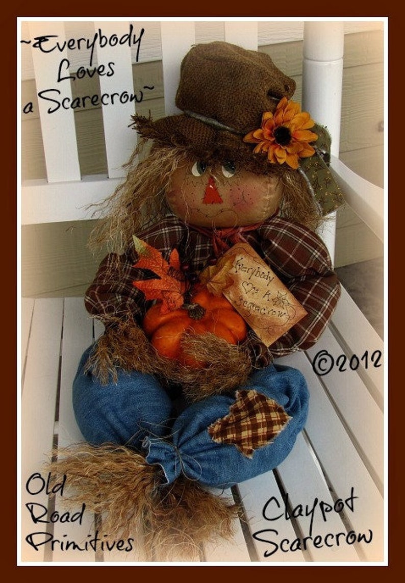 May include: A handmade scarecrow doll with a brown hat, plaid shirt, and denim overalls. The scarecrow is holding a small pumpkin and a sign that says "Everybody Loves a Scarecrow".