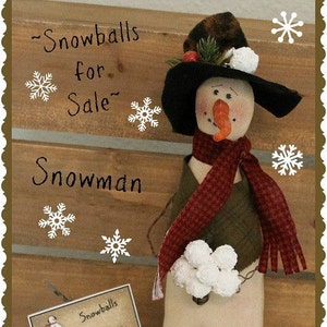 May include: A handmade snowman doll with a black hat, red and white scarf, and a green vest. The snowman is holding a bunch of white snowballs. The background is a wooden wall with the text "Snowballs for Sale" and "Snowman" written on it.
