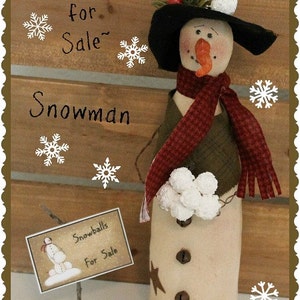 May include: A handmade snowman doll with a black hat, red and white scarf, and a sign that says "Snowballs for Sale". The snowman is holding a bunch of white snowballs. The background is a wooden wall with a rustic look.
