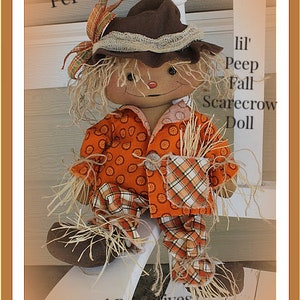 Puede incluir: Una mu&ntilde;eca de espantap&aacute;jaros de oto&ntilde;o hecha a mano con un sombrero marr&oacute;n, una camisa a cuadros naranja y blanca y pelo de paja. La mu&ntilde;eca est&aacute; sentada en una silla blanca y tiene el texto "Lil' Peep Fall Scarecrow Doll" y "Pep" escrito en la imagen.