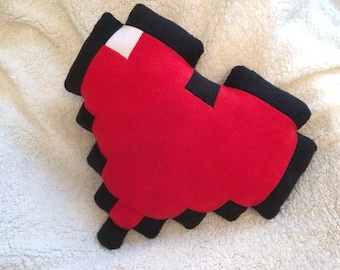 May include: A red heart-shaped pillow with black pixelated edges. The pillow is made of soft, plush fabric and is perfect for cuddling.
