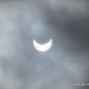 Könnte beinhalten: Eine sichelförmige Sonnenfinsternis, die durch einen bewölkten Himmel sichtbar ist.