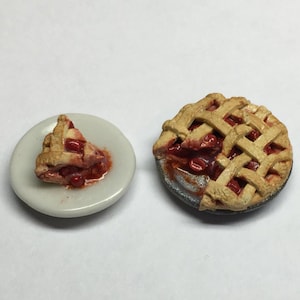 Op de afbeelding: Miniatuur kersentaart met een rasterkorst, naast een stuk op een klein wit bord. De taart heeft een goudbruine korst en een rode kersenvulling. Een charmant item met een voedselthema.