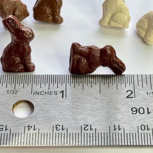 May include: A close-up of a brown ceramic bunny figurine measuring 1 inch in length. The bunny is lying on its side with its head turned to the right. The figurine is next to a ruler with inch markings.