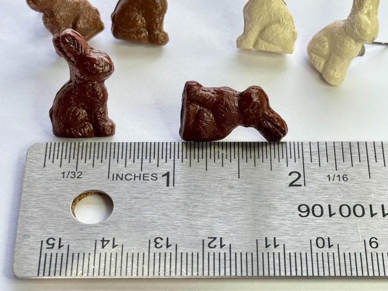 May include: A close-up of a brown ceramic bunny figurine measuring 1 inch in length. The bunny is lying on its side with its head turned to the right. The figurine is next to a ruler with inch markings.