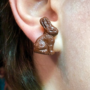 May include: A pair of brown chocolate bunny rabbit stud earrings. The earrings are a whimsical and fun accessory for any occasion.