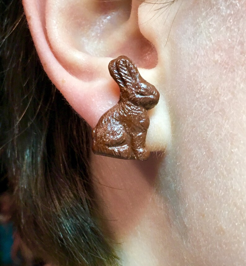 May include: A pair of brown chocolate bunny rabbit stud earrings. The earrings are a whimsical and fun accessory for any occasion.