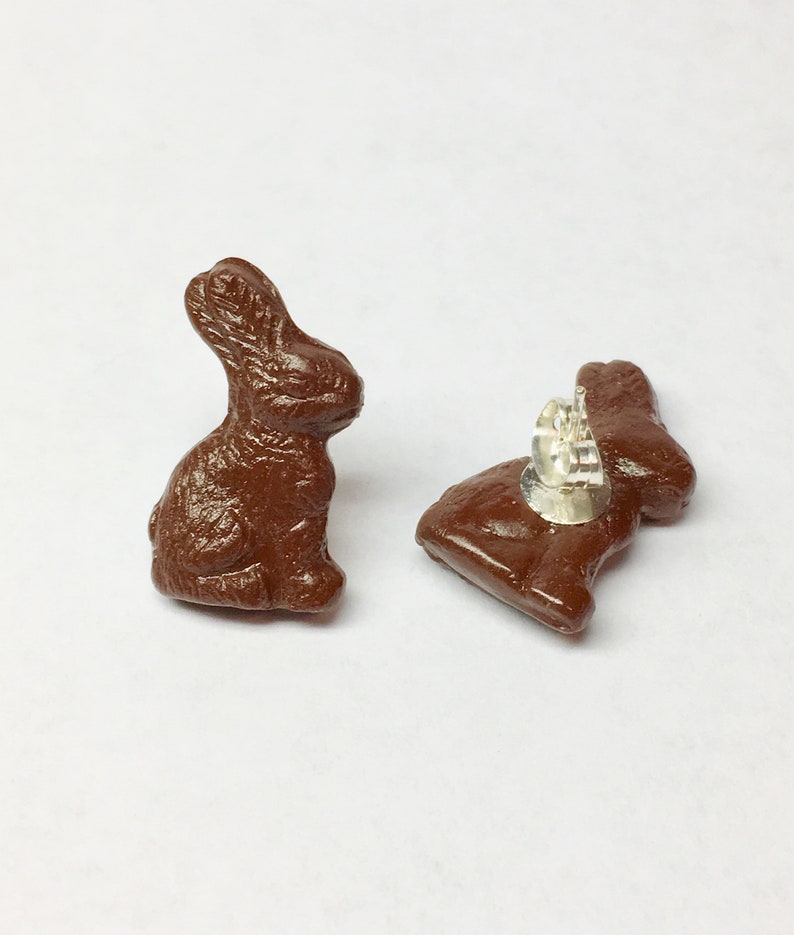 May include: A pair of brown chocolate bunny stud earrings. The earrings are made of a smooth, brown material and have a silver post.