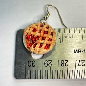 May include: A pair of cherry pie earrings, each with a red and brown pie crust and a red cherry filling. The earrings are about 1 inch in diameter and are shown next to a ruler.