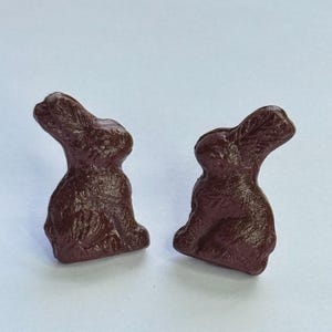 May include: A pair of brown rabbit-shaped earrings. The rabbits are sitting upright with their ears perked up.