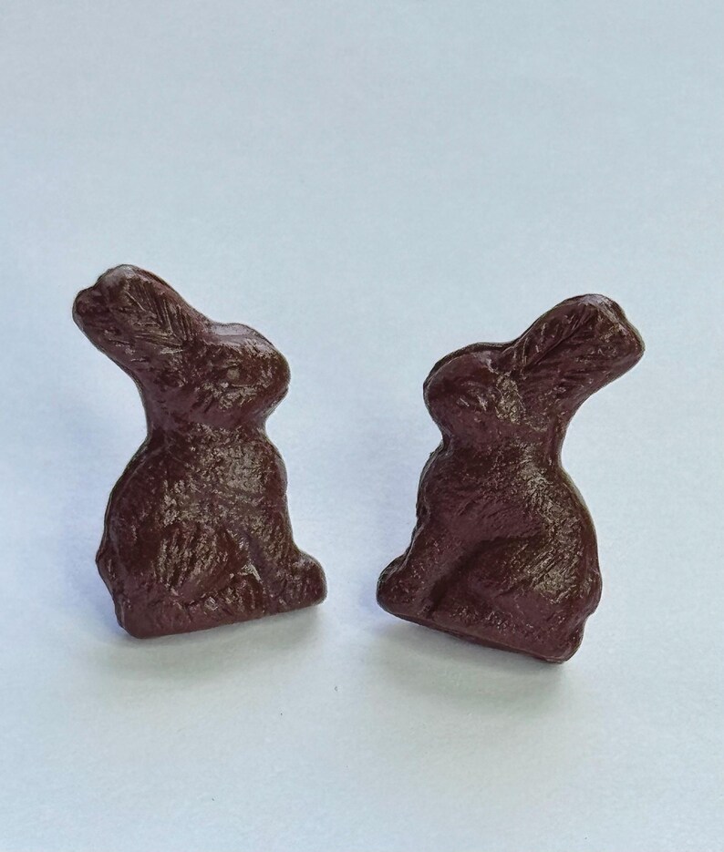 May include: A pair of brown rabbit-shaped earrings. The rabbits are sitting upright with their ears perked up.