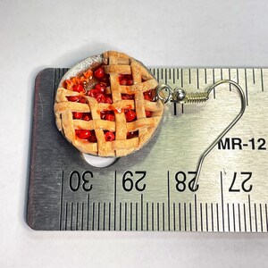 May include: A pair of cherry pie earrings with a silver hook. The pie is made of polymer clay and is about 1 inch in diameter. The earrings are shown next to a ruler.