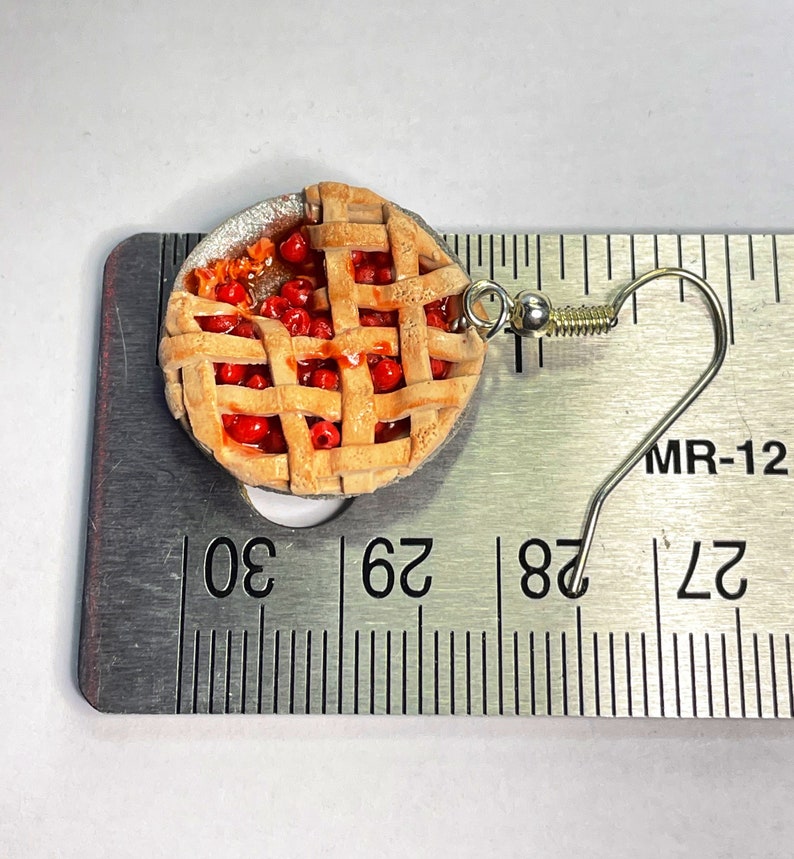 May include: A pair of cherry pie earrings with a silver hook. The pie is made of polymer clay and is about 1 inch in diameter. The earrings are shown next to a ruler.