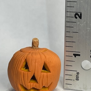 Pu&ograve; includere: Una piccola zucca di ceramica arancione con un viso intagliato e uno stelo marrone. La zucca &egrave; alta circa 2,5 cm.