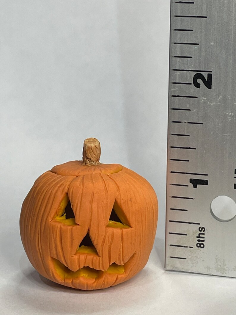 Pu&ograve; includere: Una piccola zucca di ceramica arancione con un viso intagliato e uno stelo marrone. La zucca &egrave; alta circa 2,5 cm.
