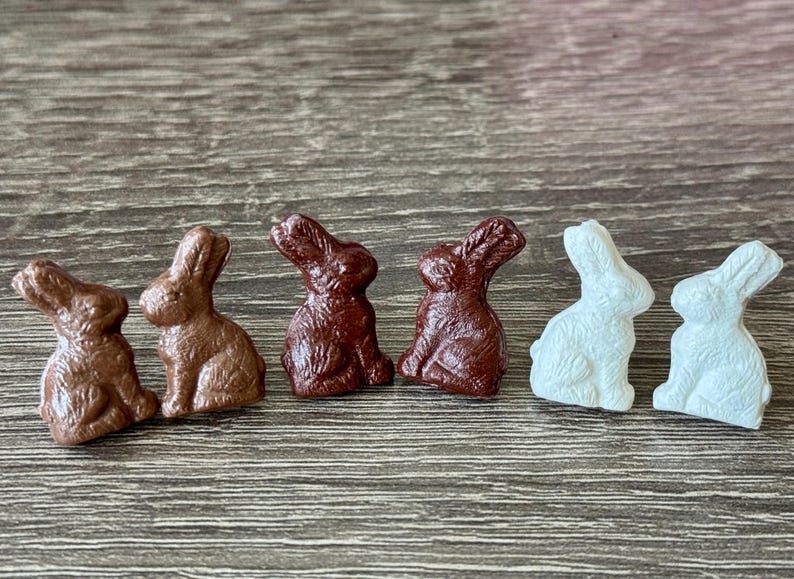 May include: Four ceramic bunny figurines, two brown and two white, arranged in a row on a wood surface. The bunnies are facing forward with their ears up.