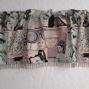 May include: A pink and green valance with a comic book print featuring women with exaggerated features and text bubbles. The valance has a brown fringe trim.
