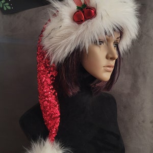 May include: A red sequined Santa hat with a white faux fur trim and pom-pom. The hat has a red bow and two jingle bells on top. The hat is on a mannequin head.