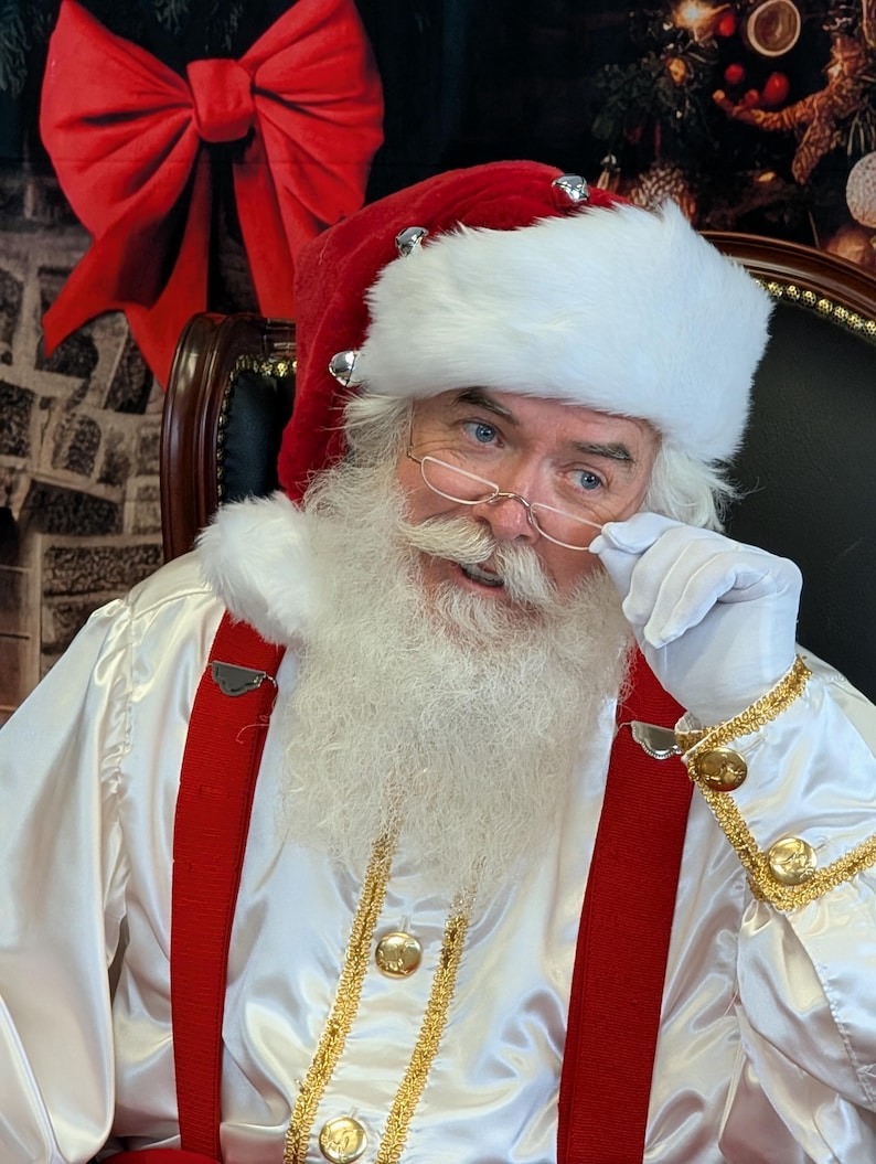 May include: A Santa Claus wearing a white fur-trimmed hat, red suit, and white gloves. He is looking at the camera and holding his glasses with his right hand. He has a white beard and mustache.