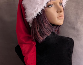 Può includere: Un lungo cappello da Babbo Natale in velluto rosso con un bordo spesso in pelliccia sintetica bianca e un pon-pon in pelliccia sintetica abbinato sulla punta. Il cappello è esposto su una testa di manichino, con il testo originalsbyeva.etsy.com.