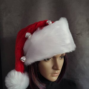 May include: A white faux fur Santa hat with a red pom pom and red trim. The hat has silver jingle bells attached to the brim.