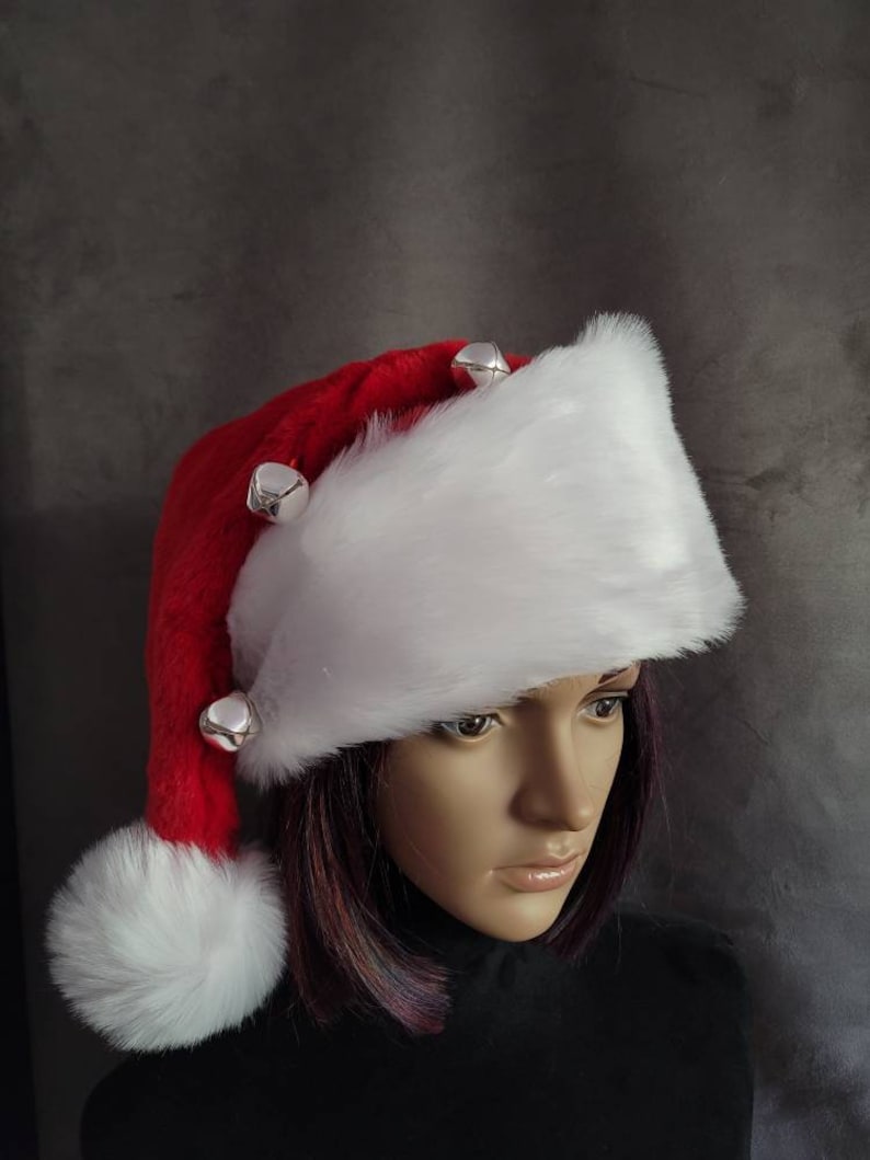 May include: A white faux fur Santa hat with a red pom pom and red trim. The hat has silver jingle bells attached to the brim.