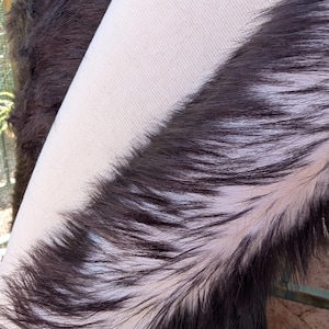 May include: Close-up of a black and white fur texture. The fur is long and soft, with a white stripe running down the center.