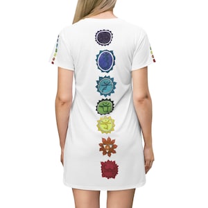 May include: White t-shirt dress featuring a vertical design of seven colorful chakra symbols down the back. The symbols are in shades of purple, blue, green, yellow, orange, and red. The sleeves have small, colorful floral designs.