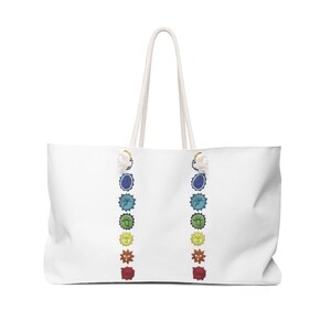 May include: White canvas tote bag with a colorful chakra design. The bag has two white rope handles and features seven chakras with their corresponding colors and symbols.