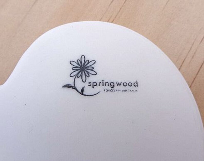K&ouml;nnte beinhalten: Ein wei&szlig;er Keramikteller mit einer stilisierten schwarzen und wei&szlig;en Blume und dem Text "Springwood Porcelain Australia".