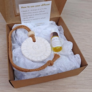 May include: Aromatherapy diffuser set in a brown box. The set includes a white ceramic diffuser with a brown rope, a small bottle of essential oil, and a card with instructions. The essential oil bottle is labelled "Bush Walk Eucalyptus Sweet Orange Cedarwood."
