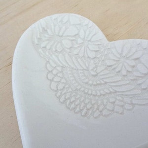 K&ouml;nnte beinhalten: Wei&szlig;e, herzf&ouml;rmige Schale aus Keramik mit einem gepr&auml;gten Blumenmuster.