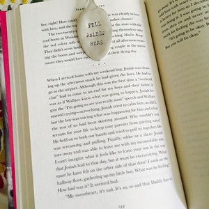 May include: A close-up of a silver spoon bookmark with the words "Fell Asleep Here" engraved on it. The bookmark is placed on a page of a book with text about a father and son.