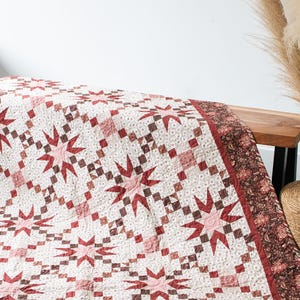 May include: A red and white quilt with a starburst pattern. The quilt is made of cotton fabric and has a brown border.