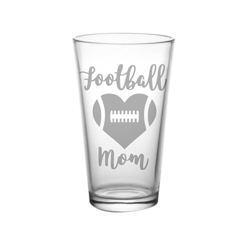 May include: A clear glass pint glass with a gray design that says "Football Mom" with a heart and a football inside the heart.