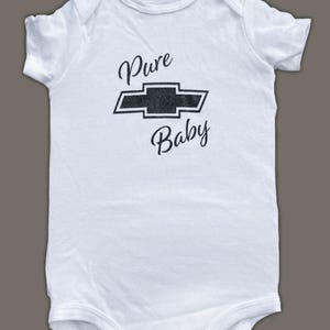 K&ouml;nnte beinhalten: Wei&szlig;er Baby-Strampler mit einem schwarzen Chevrolet-Logo und dem Text "Pure Baby" auf der Vorderseite.