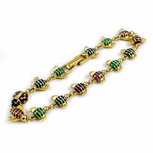 May include: A gold bracelet with a chain link design features a series of colorful enamel ladybug charms. The ladybugs are decorated with green, red, blue, and black stripes.