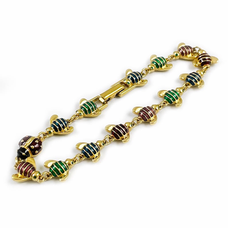 May include: A gold bracelet with a chain link design features a series of colorful enamel ladybug charms. The ladybugs are decorated with green, red, blue, and black stripes.